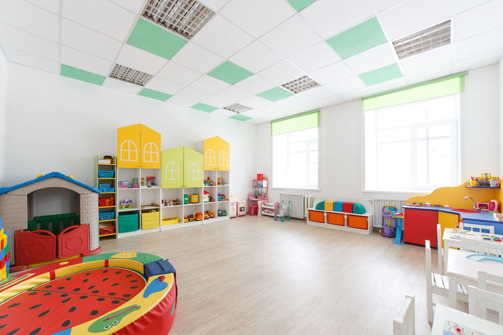 Spacious bright game room in the kindergarten with toys, two large windows and tables for classes. Natural light.